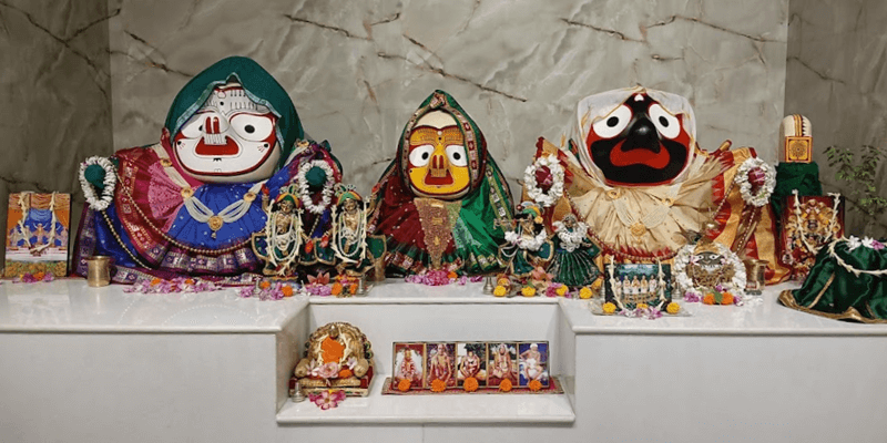 The temple altar: Lord Jagannath, Lord Baladeva and Subhadra Devi, dressed in bright cloth and flower garlands, with smaller deities and pictures of the spiritual masters